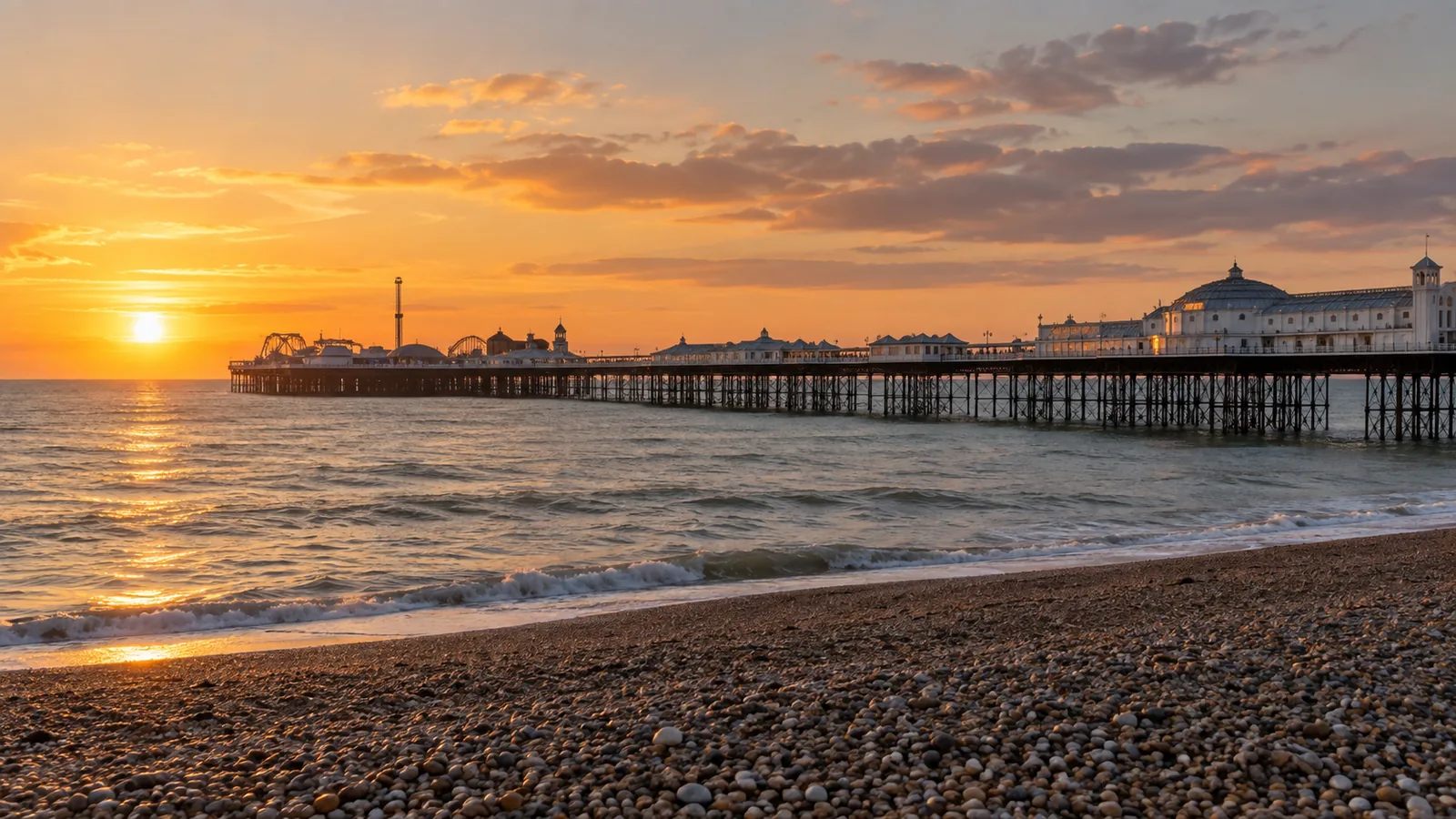 Brighton Palace Pier extending into the sea at golden-hour sunset with a pebble beach in the foreground